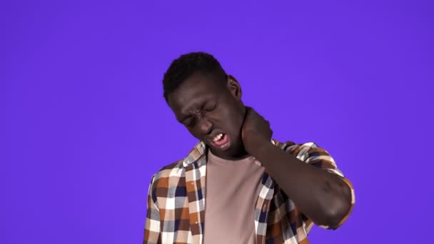 Joven hombre afroamericano en camisa a cuadros con dolor de cuello o súper cansado, mueca de la cara. Aislado sobre fondo azul — Vídeos de Stock