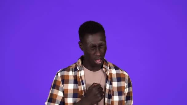 Kranker junger afrikanischer Mann hustet stark und schlägt sich isoliert auf blauem Hintergrund auf die Brust. Im karierten Hemd — Stockvideo