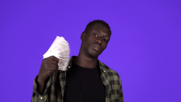 Glücklicher afrikanisch-amerikanischer Mann hält Hundert-Dollar-Banknoten-Fan, nickt und blickt in die Kamera, während er vor blauem Hintergrund im Studio posiert — Stockvideo