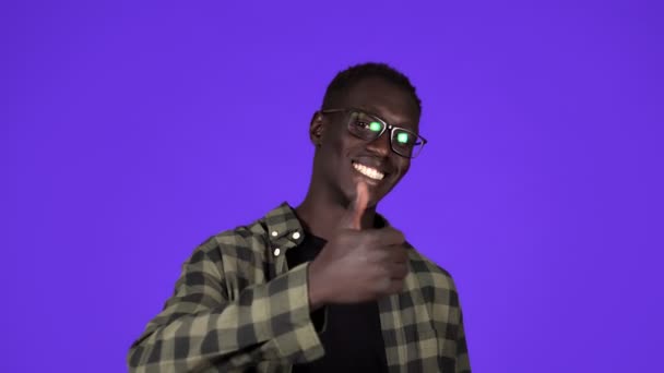 Glücklicher, lächelnder afrikanisch-amerikanischer Mann in guter Laune auf blauem Hintergrund. Mann in stylischem Glanz gestikuliert mit erhobenem Daumen, wie Geste und lächelndes Spielzeug - menschliche Emotionen — Stockvideo