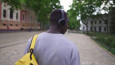 Güzel, eski bir şehirde kulaklık ve akıllı telefon kullanarak müzik dinleyen Afrikalı Amerikalı genç turistlerin nadir görüntüsü. Sarı sırt çantası, siyah kulaklıklar mutluluk caddesi çekici yavaş çekim