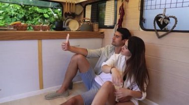 Güzel bir çift karavanda şık bir mutfakta yerde oturmuş akıllı telefon kullanarak, poz vererek selfie çekiyorlar. Beraberliğin tadını çıkarmak, tatilleri paylaşmak, tekerlekli sandalyeyle seyahat etmek. Modern iç mimari