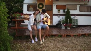 Evlerinin önünde oturan mutlu, rahat bir çift ve kız arkadaşı için gitar çalan bir adam. Açık havada. Müzik dinleyen ve sarılan bir kız. Ağır çekim. Ön görünüm