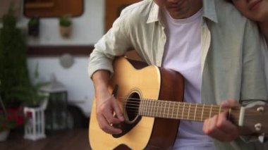 Evlerinin önünde oturan romantik, güzel bir çift ve kız arkadaşı için gitar çalan bir adam. Açık havada. Müzik dinleyen bir kız, omzuna yaslanmış.