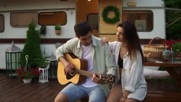 Evlerinin önünde oturan romantik bir çift ve kız arkadaşı için gitar çalan bir adam. Açık havada. Kız müzik dinliyor ve sarılıyor. — Stok video