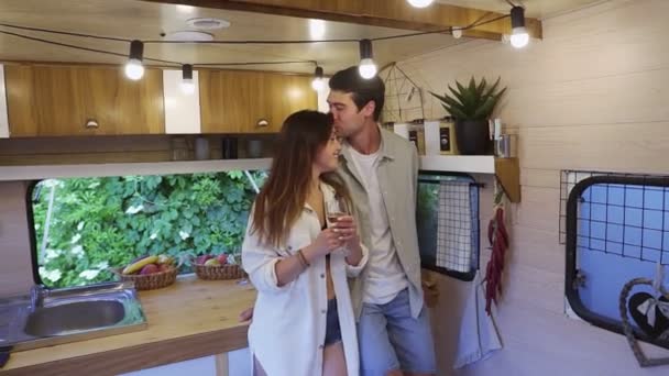 Pareja feliz disfrutando del tiempo juntos en una pequeña cocina en furgoneta. Familia marido y mujer bebiendo, celebrando aniversario romántico juntos, besándose en las ruedas casa de vacaciones — Vídeos de Stock