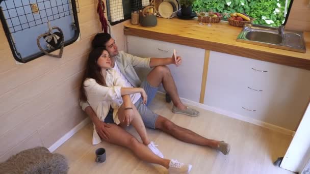 Hermosa pareja sentada en el suelo en la elegante cocina en furgoneta y haciendo selfie usando un teléfono inteligente, posando. Disfrutando juntos, vacaciones compartidas, viajando por la casa de ruedas. Interior moderno. Alto. — Vídeo de stock