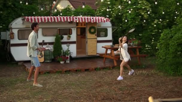Two young tourist couple play badminton next to their trailer in american retro style. Active vacation, rest, traveling. Summer, warm day — Stock Video