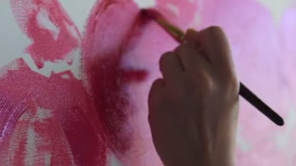 Close-up de artista irreconhecível pinta peônias vermelhas ou outras flores com escova na tela. O artista pinta flores cor-de-rosa sobre tela com pincel grosso, close-up, vista lateral. Luz natural do sol deitado — Vídeo de Stock