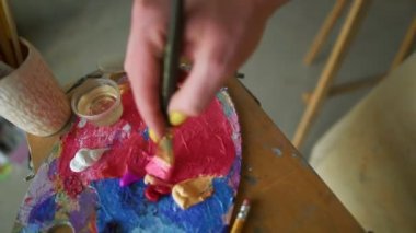 Ressam bir resim yapmadan önce palette pembe boya karıştırıyor, stüdyoda ressam, yaratıcı sanat eseri yapıyor. Geniş fırçalı kadın eli, tuvale yağlı boya sürüyordu.