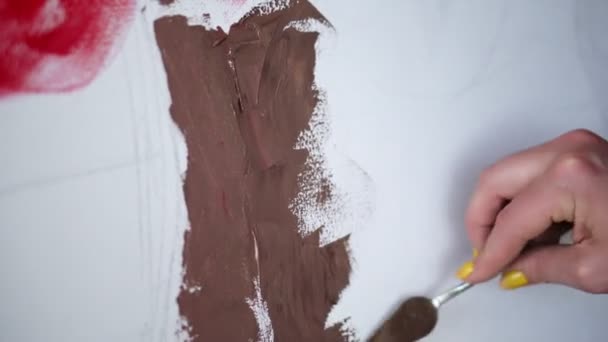 Неузнаваемые художники рисуют, создавая новые произведения искусства на холсте. Художник рисует шпателем, шпатлевочным ножом, нанося коричневую краску на белый холст. Закрыть — стоковое видео