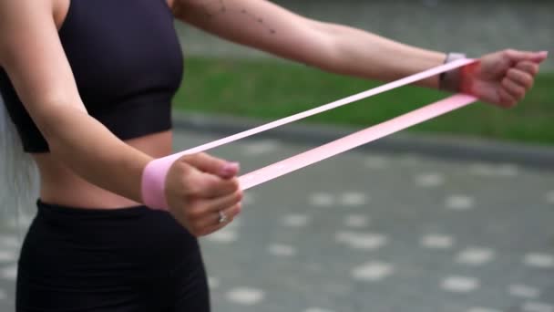 Onherkenbaar atletisch meisje dat zich bezighoudt met fitness en zwarte sportkleding draagt met een elastiekje in haar handen in een zomerpark. Meisje met kleine tatoeage bij de hand oefenen alleen in de ochtend — Stockvideo