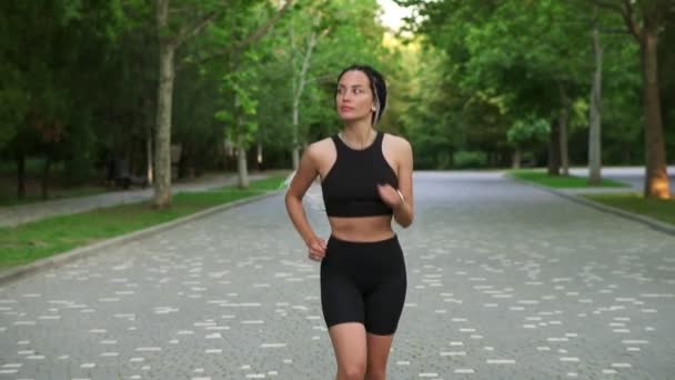Front view of european woman with black and white dreadlocks running by local, green park in the city. She is exercising for good health. Wearing black top and shorts. Slow motion — Stock Video