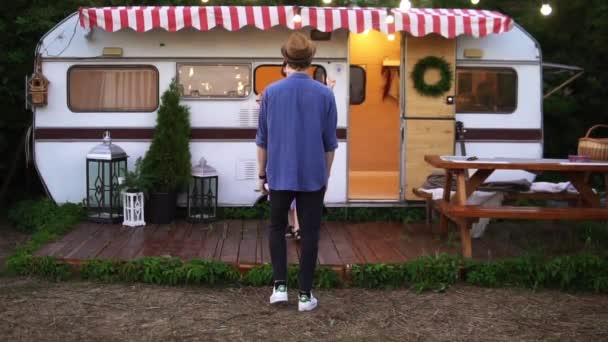 Mooi stel dat plezier heeft in de buurt van een trailer in het park, slank meisje dat in de armen van haar vriendje springt en haar ronddraait. Perfecte foto van vrolijk, jong stel op vakantie. Vooraanzicht — Stockvideo