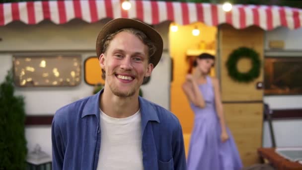 Glada glada glada par - porträtt av en man i hatt ler åt förgrunden, kvinna har roligt, dansa tillsammans på tröskeln hus på hjul utomhus på suddig bakgrund. Retrostil exteriör. Långsamt — Stockvideo