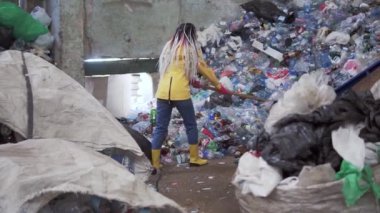 Sarı çizmeli, rastalı bir kızın ender görülen görüntüsü. Plastik geri dönüşüm fabrikasında büyük ördek kürekleriyle dolu şişeler kullanılmış. Arka planda koca bir şişe yığını