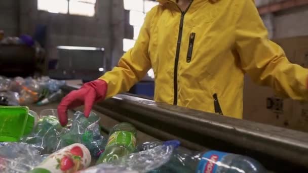 Unbekannter in gelber Jacke und Handschuhen sortiert gebrauchte Plastikflaschen auf Recyclinganlage. Flaschen auf der Linie trennen, zusammendrücken und in den Karton legen — Stockvideo