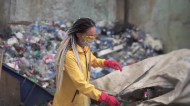 Sarı ve şeffaf koruma bardakları içinde gönüllü bir kadın modern geri dönüşüm fabrikasında kullanılmış plastik şişeleri ayırıyor. Ayrı çöp toplama yeri. Çöp Sıralama