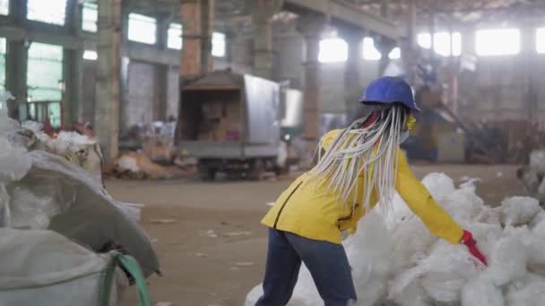 Atık işleme tesisi. Teknolojik süreç. Daha fazla atık için geri dönüşüm ve depolama. Geri dönüşüm fabrikasındaki kullanılmış plastik bantlara basan, kasklı kadın işçi. — Stok video