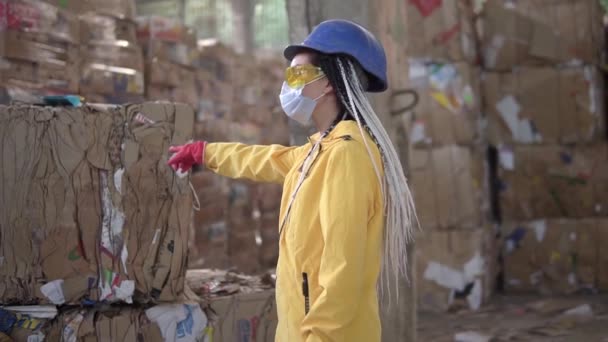 Déchargement de vieux papiers dans un entrepôt de contrôle de voiture électrique par des travailleuses en casque et veste jaune. D'énormes stocks de carton pressé. Femme pointant sur une pile particulière. Mouvement lent — Video