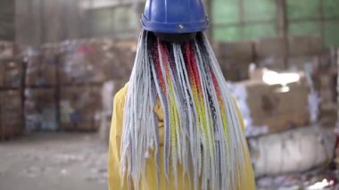 Atık işleme tesisi. Daha fazla atık için geri dönüşüm ve depolama. Sert şapkalı kadın işçi, eldivenler çöp öğütücülerin arasında yürüyor, büyük kazıklar. Nadir görüntüler