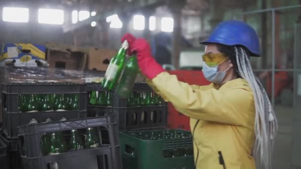 Frau in Maske arbeitet an der Recyclingabfalltrennung von Wertstoffanlagen. Sortieren und Ordnen von Glasflaschen in Schachteln zur weiteren Entsorgung. Zeitlupe — Stockvideo