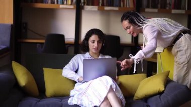 Ev ofisinde dizüstü bilgisayarla çalışan bir iş kadını. Bilgisayar üzerinde çalışan genç bir bayan profesyonel. Arkaplanda kitaplar olan kitaplıklar. Kulaklıkla kanepede oturuyor, arkadaşı gülümseyerek...