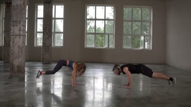 Man och kvinna med dreadlocks i fitness studio gör övningar tillsammans, utför armhävningar med hopp och klappar. Loft inredning. Sidovy — Stockvideo