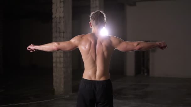 Sterke bodybuilder poseren achterkant na de training met spotlight lens flare - tonen zijn lichaam en spieren verspreiden van de handen — Stockvideo