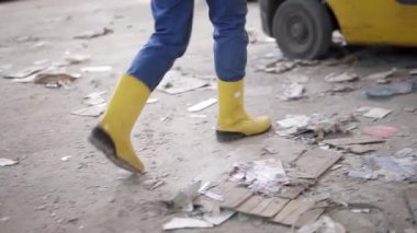 Elektrikli bir depoya atık kağıt boşaltıyorum. Kasklı ve sarı ceketli bir kadın makinede oturuyor. Büyük miktarda basılmış karton. Kadın sürücü, sıkıştırılmış Corton destelerini ayırıyor.