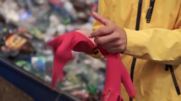 Close up view of woman standing indoor put red rubber protective gloves on hands. Caution preventive measures working with dirt. Self care, personal safety. Pile of used plastic bottles on blurred — Stock Video