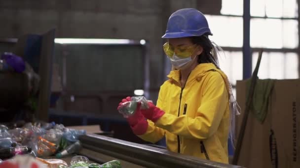 在回收厂，女志愿者戴着黄色透明的保护眼镜和面罩，对用过的塑料瓶进行分类。将瓶口分开，取出瓶盖，挤压 — 图库视频影像