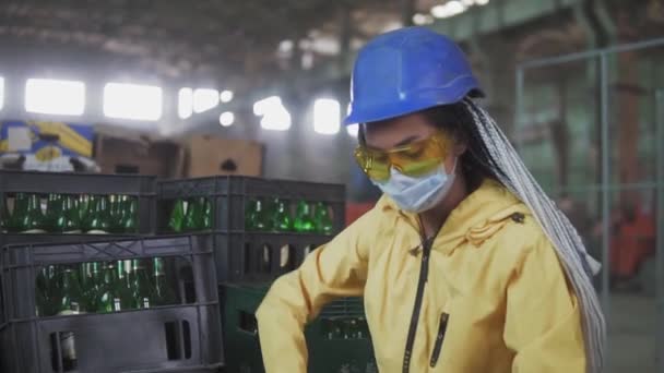 La mujer trabajadora en máscara controla la separación de residuos reciclables de las plantas de residuos reciclables. Clasificación de botellas de vidrio en cajas para su posterior eliminación. Movimiento lento — Vídeo de stock