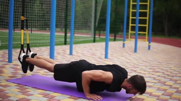 Hombre europeo haciendo flexiones en la estera usando cinturones deportivos colgando piernas para fortalecer el ejercicio al aire libre — Vídeos de Stock