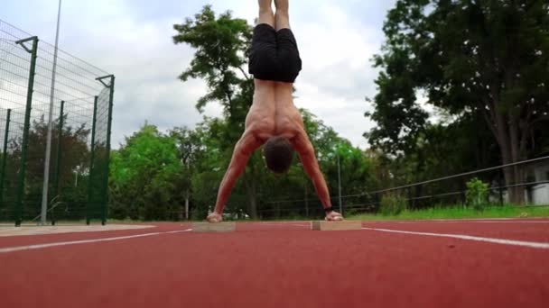 Un athlète torse nu se tient à l'envers appuyé sur des supports spéciaux sur la piste de course à l'extérieur — Video