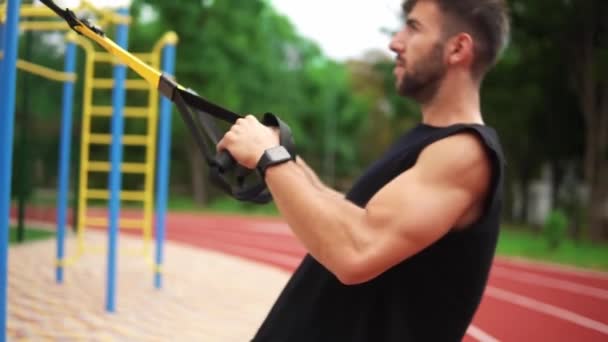 Um homem atlético fazendo exercícios push-ups usando cinto de borracha para forçar o décimo do treino nos músculos do peito e bíceps — Vídeo de Stock