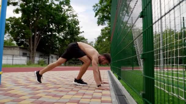 Un atleta sta facendo flessioni sulle mani in piedi a testa in giù vicino al muro all'aperto. Giovane uomo in topless in pantaloncini neri — Video Stock