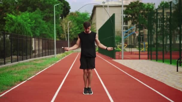 Fit, homem barbudo em pé na pista de corrida ao ar livre no estádio moderno fazendo exercício com pular corda — Vídeo de Stock