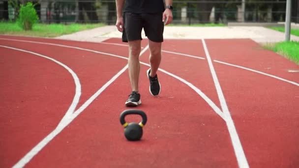 Primer plano de imágenes de un hombre en ropa deportiva negro viene a entrenar con pesas al aire libre en la pista de carreras al aire libre — Vídeos de Stock