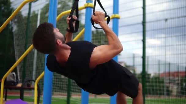 Μυώδης αθλητής κάνει κρέμονται pull ups άσκηση χρησιμοποιώντας ζώνη τακτοποίησης για να αναγκάσει την ένταση της άσκησης σε εξωτερικούς χώρους — Αρχείο Βίντεο