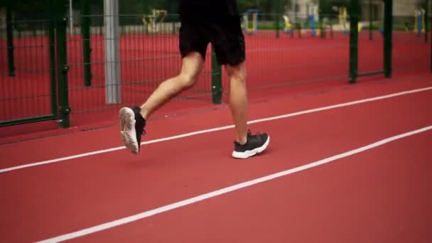 Close up de pernas masculinas, um atleta está correndo em pista de corrida no estádio de atletismo — Vídeo de Stock