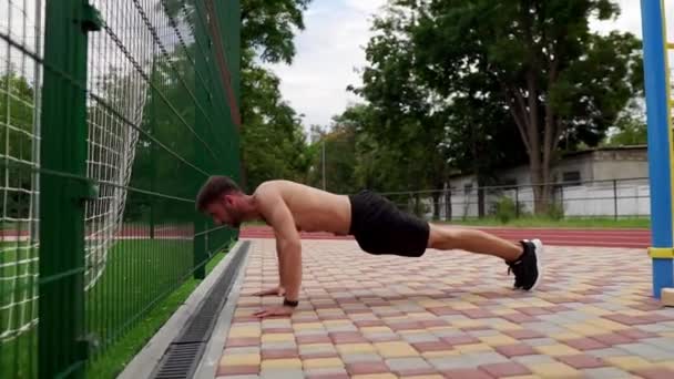 Hombre en pantalones cortos negros, sin camisa haciendo flexiones en suelo pavimentado al aire libre — Vídeos de Stock