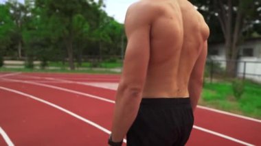 Yorgun, üstsüz bir adam antrenmandan sonra stadyum yarışına çıkıyor.