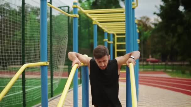 Musculaire man doet push-ups op crossbar buiten op het stadion in de zomer — Stockvideo