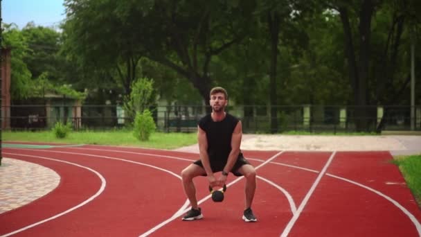 Um homem de trem sportswear preto com peso bob ao ar livre perto do estádio na pista de corrida — Vídeo de Stock