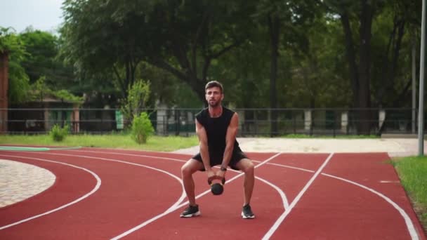 Um homem de trem sportswear preto com peso bob ao ar livre perto do estádio na pista de corrida em slowmo — Vídeo de Stock