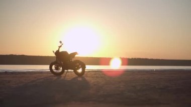 Gün batımında suya yakın arka planda su hattı olan bir motosiklet parkı. Düşük açı görünümü