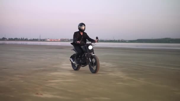 Onherkenbare jonge biker in helm en jas, man is rijden op sport motor. Wind waait, waterkant — Stockvideo