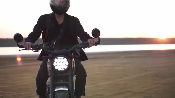 Close up de motociclistas passeio em bicicleta esporte preto com farol dianteiro comutado. À beira-mar, pôr do sol — Vídeo de Stock