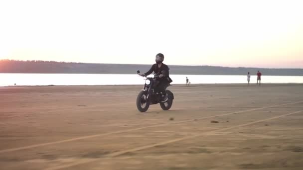 Motociclista en casco y chaqueta, el hombre está montando en moto deportiva. Soplado de viento, frente al agua, puesta de sol — Vídeos de Stock